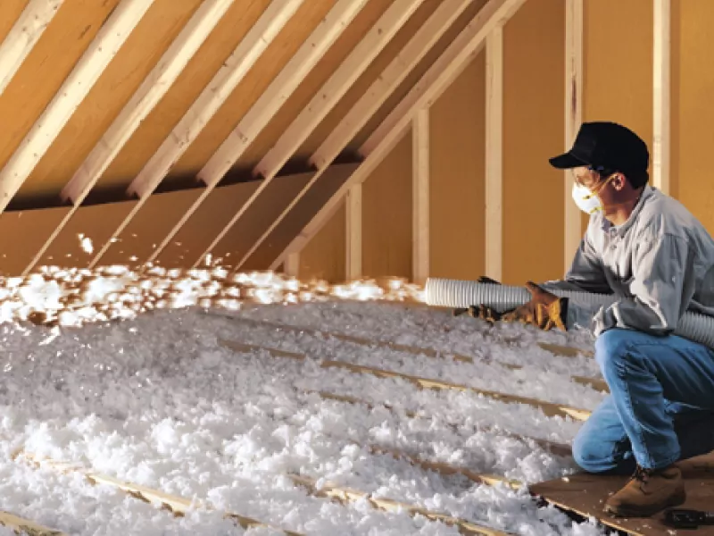 Worker installing blown-in insulation in an attic.