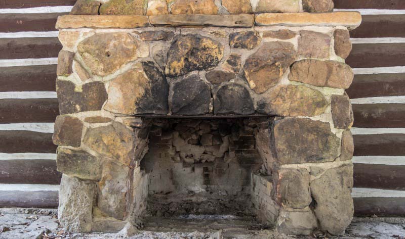Rustic stone fireplace in a log cabin room with an empty firebox