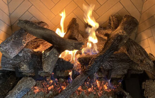 Close-up of gas logs burning in a herringbone brick fireplace with bright flames