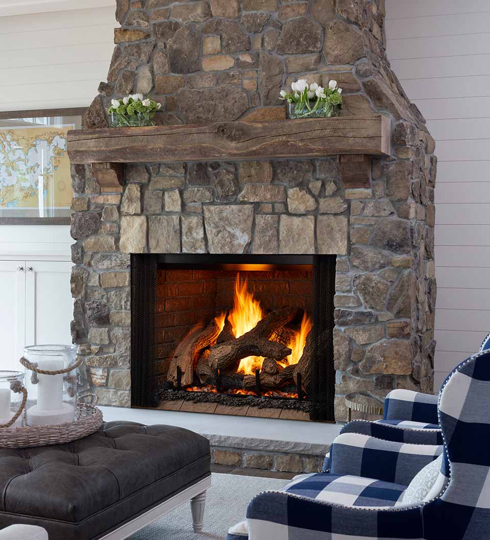 Traditional stone fireplace with rustic mantel and gas log set burning brightly in a brick-lined firebox.