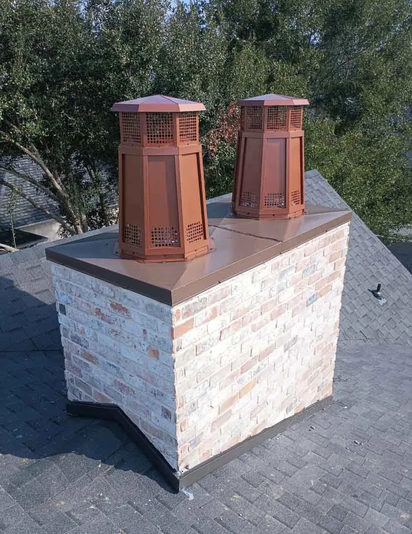 Brick chimney chase with two copper chimney caps on an asphalt shingle roof.