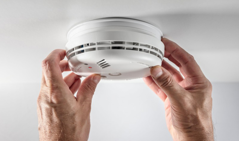 Close-up of hands installing a white smoke detector on a ceiling.
