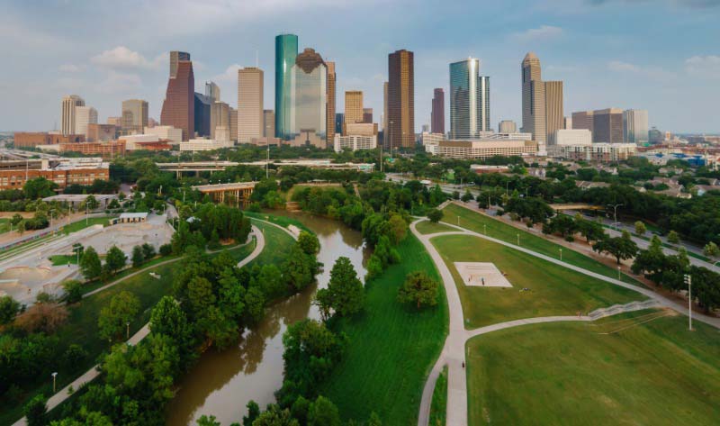 Aerial view of downtown Houston Texas skyline with Buffalo Bayou Park and green trees in the foreground.