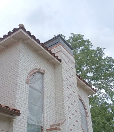 Close-up of custom decorative chimney upper installed on a white brick chimney. Close-up of custom decorative chimney upper installed on a white brick chimney with red brick accents on a Spanish-style home with clay tile roof