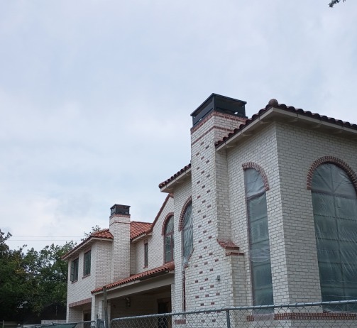 Wide exterior view of a Spanish-style white brick home with multiple chimneys. Wide exterior view of a Spanish-style white brick home with multiple chimneys each fitted with custom decorative chimney uppers, arched windows, and a clay tile roof.