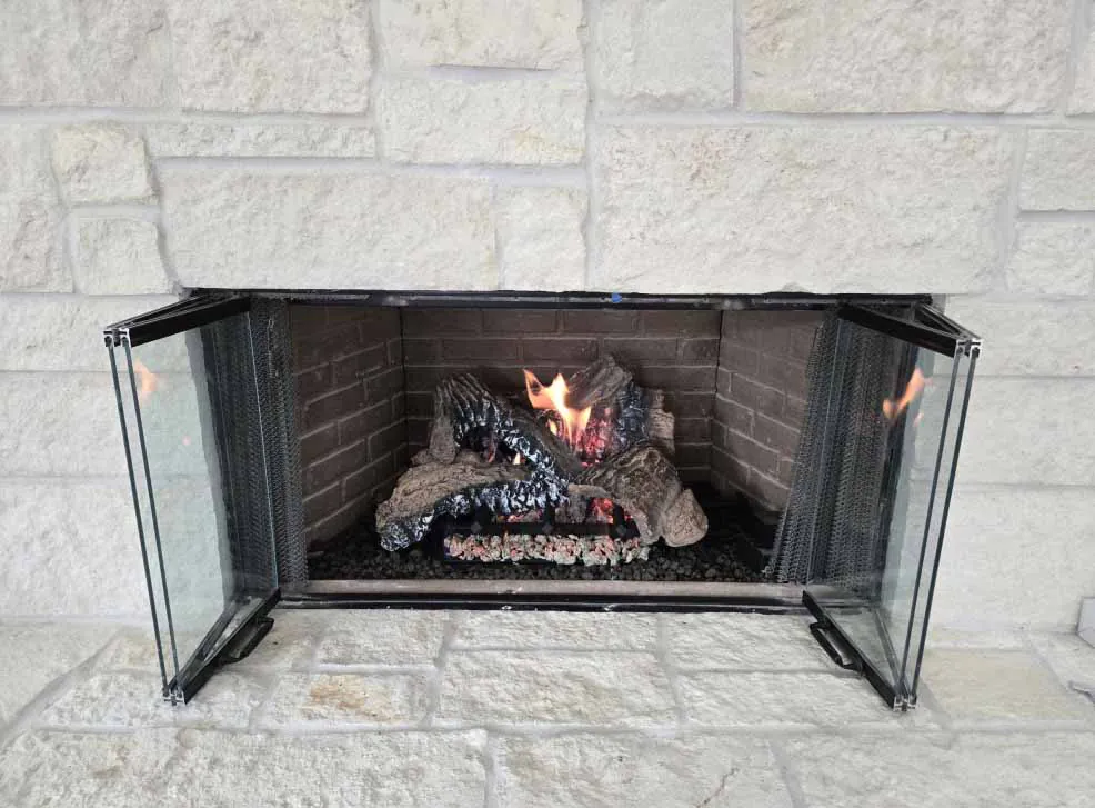 Duzy 2 remote control gas log set burning in a brick-lined fireplace. Duzy 2 remote control gas log set burning in a brick-lined fireplace with glass door screen and white stone surround.