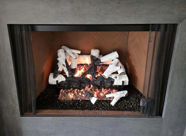 Close-up of Grand Birch 30-inch 3-tier remote control gas log set. Close-up of Grand Birch 30-inch 3-tier remote control gas log set burning with glowing embers inside a fireplace with herringbone tile interior and modern concrete surround.