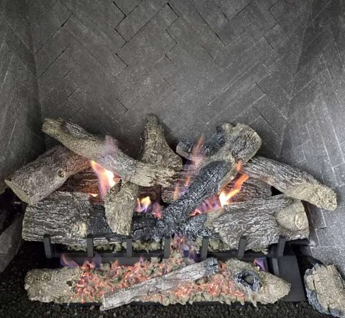 Close-up of Grand Oak 2-Tier 30-inch remote control gas log set Close-up of Grand Oak 2-Tier 30-inch remote control gas log set with flames burning between realistic oak logs on a herringbone-tiled fireplace interior.