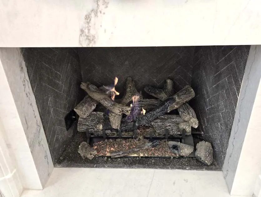 Grand Oak 2-Tier 30-inch remote control gas log set Grand Oak 2-Tier 30-inch remote control gas log set burning inside a fireplace with dark herringbone tile interior and white marble surround.