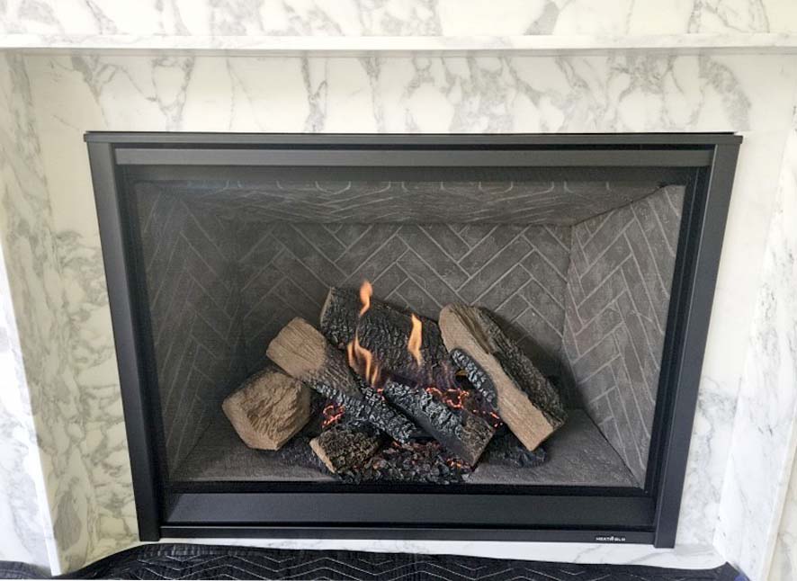 Heat & Glo 8KX 42-inch direct vent gas fireplace. Heat & Glo 8KX 42-inch direct vent gas fireplace with tranquil greige herringbone interior panels, folio mesh screen front, and gas logs burning against a white marble surround.