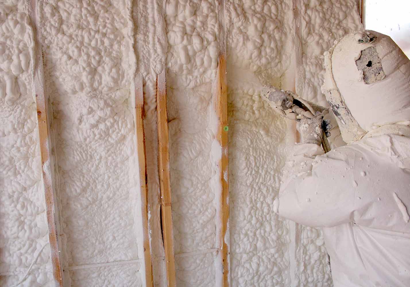 Technician applying Quadrant open-cell spray foam insulation to wall stud cavities, installed by Perfection Supply, Houston, TX.