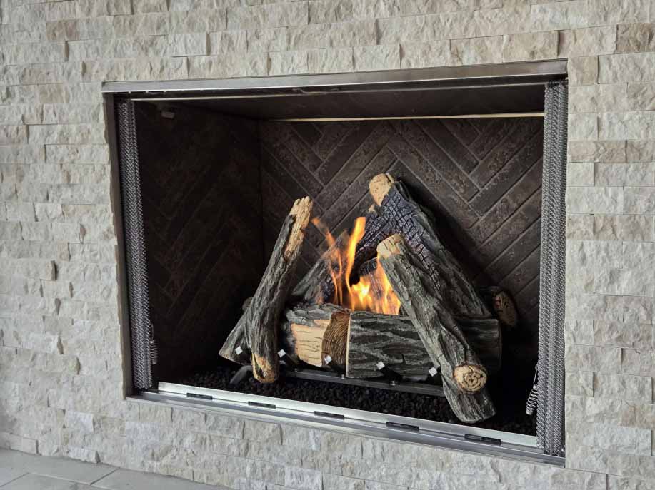 Close-up of a Courtyard 42-inch outdoor gas fireplace with a high-definition log set. Close-up of a Courtyard 42-inch outdoor gas fireplace with a high-definition log set, brown herringbone interior panels, and mesh screen in Cypress, TX.