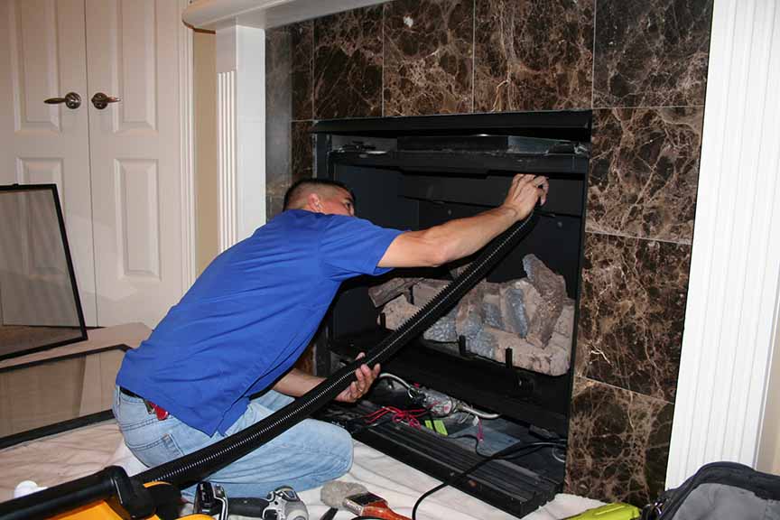 Perfection Supply technician vacuuming dust and debris from inside a gas fireplace firebox during a pre-season tune-up in Houston, TX.