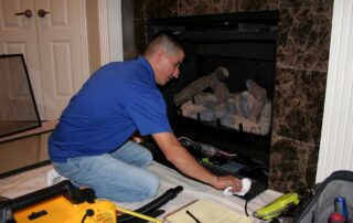 Perfection Supply technician wiping down the lower louver of a gas fireplace with the log set in place during a pre-season tune-up in Houston, TX.